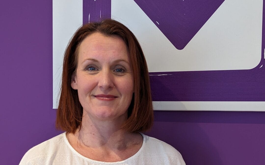 The Clinical Director of the Purple House Clinic Edinburgh standing in front of the Purple House Clinic logo, smiling.