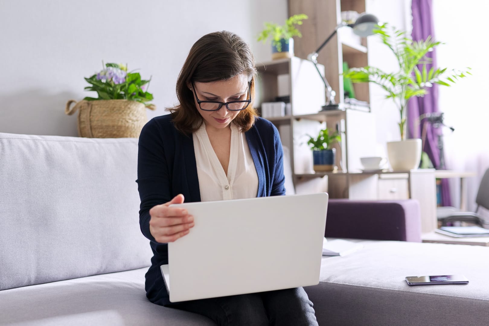 Cozy Online Therapy Session with Purple House Clinic A person sitting on a sofa using a laptop, with plants in the background, illustrating a cozy online therapy session setup.