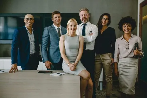 Group of business executives smiling in front of desk/table representing the Purple House Clinic's Employee Wellbeing Service