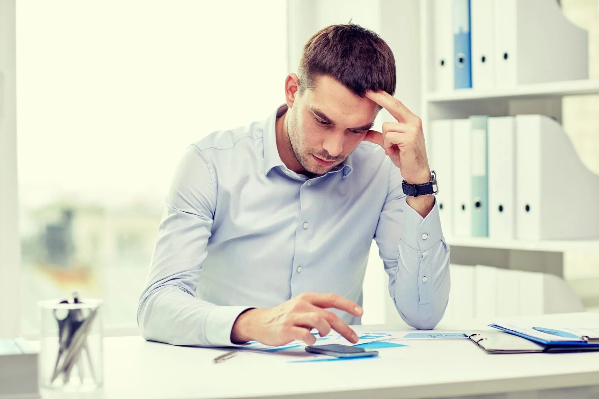 Businessman in office experiencing work stress, looking concerned at paperwork.