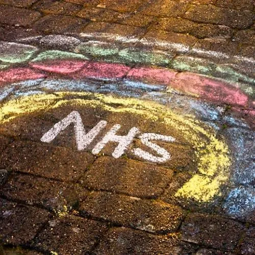 A chalk drawing on cobblestones, of a colourful rainbow with 'NHS' in white chalk underneath.