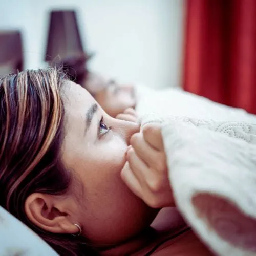 A woman lying in bed with the covers up around her face, looking scared - representing the Purple House Clinic's Psychosexual Therapy Service.