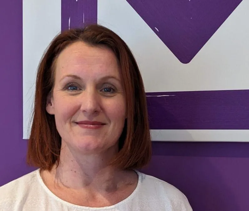 The Clinical Director of the Purple House Clinic Edinburgh standing in front of the Purple House Clinic logo, smiling.